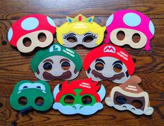 six masks with different designs on them sitting on top of a wooden table next to each other