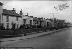 an old black and white photo of houses on the side of a street with a fence