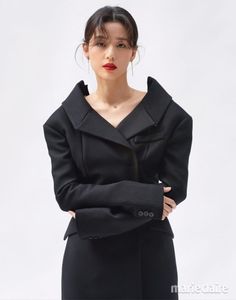 a woman wearing a black coat and red lipstick standing with her hands on her hips