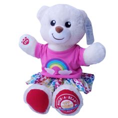 a white teddy bear with a pink shirt and rainbow skirt sitting on a white background