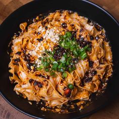 a black bowl filled with noodles and vegetables on top of a wooden table next to a fork