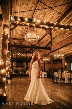 a woman in a wedding dress standing on a wooden floor with lights hanging from the ceiling