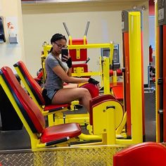 a woman sitting on top of a yellow machine in a gym with red and yellow chairs