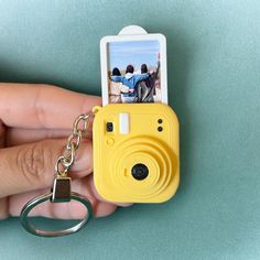 a hand holding a yellow camera keychain with a photo attached to the front