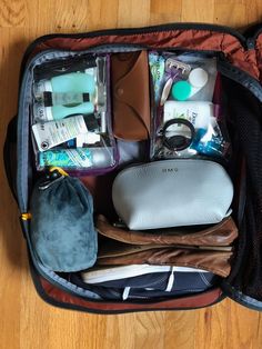 an open suitcase filled with personal care items on a wooden floor next to a handbag