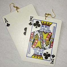 two playing cards sitting next to each other on top of a white table with gold earrings