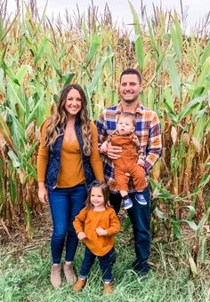 a man, woman and child standing in front of a cornfield with the baby holding him