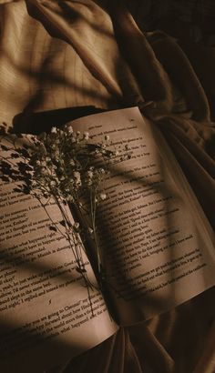 an open book sitting on top of a bed next to a bouquet of wildflowers