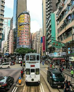 a white double decker bus driving down a street next to tall buildings and parked cars