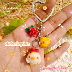 a hand holding a keychain with two little chickens on it and a flower in the middle