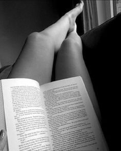 a person reading a book while laying down on a couch with their legs crossed and feet propped up