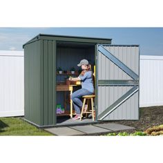 a woman sitting at a table in a shed with the door open and she is leaning on a stool