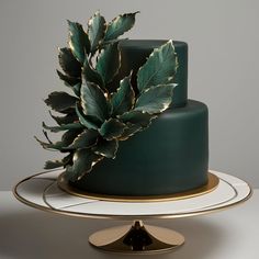 there is a green cake with gold trim and a plant on the top of it