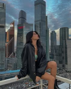 a woman sitting on top of a metal railing next to tall buildings in the city