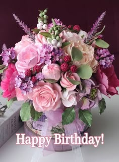 a birthday card with pink flowers and greenery in a basket on a table next to a book