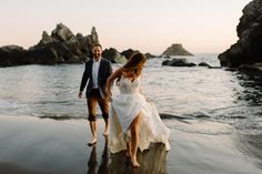 a bride and groom walking on the beach at sunset with their feet in the water