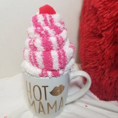 a hot chocolate cup with pink and white frosting on top sitting next to a red pillow