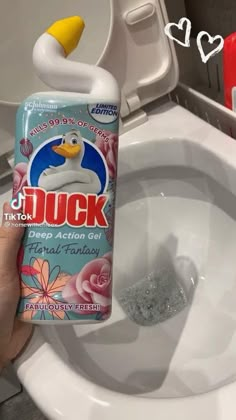 a hand holding a bottle of duck deodorant next to a toilet