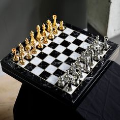 a chess board with gold and silver pieces on it, sitting on a black table