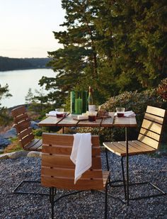 an outdoor table with two chairs and a bottle of wine on it, in front of some rocks