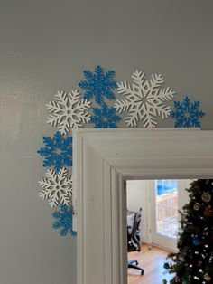 snowflakes are hanging on the wall in front of a mirror and christmas tree