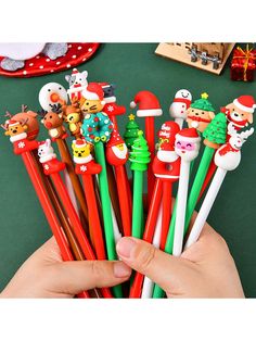 a hand holding several christmas themed pencils in front of a green table with other items on it