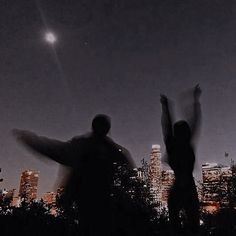 two people standing in front of a city skyline at night with their arms raised up