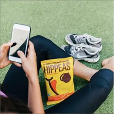 a woman sitting on the ground with her cell phone next to a bag of hipeas