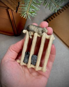 a hand holding a small toy animal in it's cage next to a pine tree