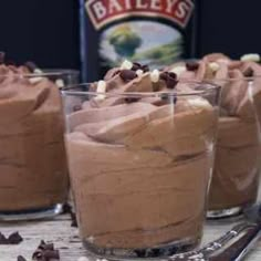 three glasses filled with chocolate desserts on top of a wooden table next to a bottle of bailey's