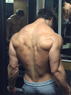 a man standing in front of a mirror with his back turned to the camera and no shirt on