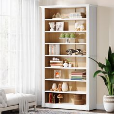 a living room with a white bookcase filled with lots of books and plants next to a window