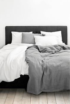 an unmade bed with white sheets and grey linens in a minimalistic bedroom