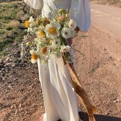 a woman holding a bouquet of flowers in her hand on the side of a dirt road