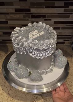 a silver cake sitting on top of a metal plate next to a person's hand