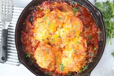 a skillet filled with meat covered in cheese and tomato sauce next to a fork