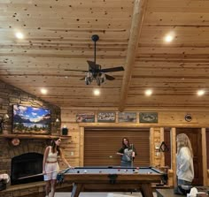 a man and woman playing pool in a living room with wood paneling on the ceiling