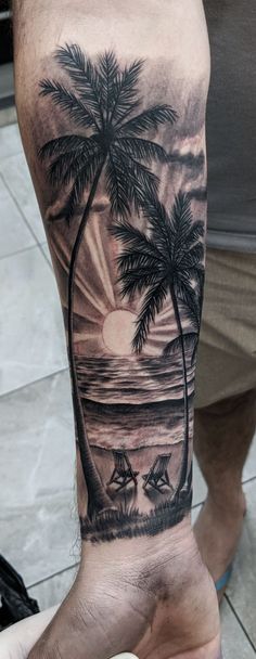 a man's arm with a palm tree and sailboats on the beach at sunset