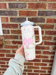 a person is holding up a pink and white coffee cup in front of a brick wall