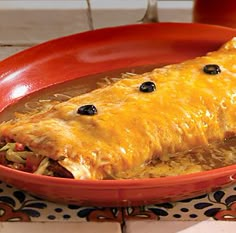 an enchilada in a red dish with black olives