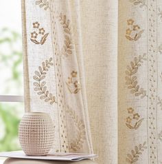 a white vase sitting on top of a table next to a window covered in curtains