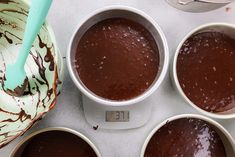 four white bowls filled with chocolate pudding on top of a counter next to a measuring cup