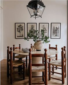 a dining room table with chairs and pictures on the wall above it, along with two vases filled with flowers