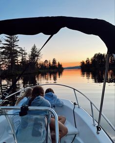 two people are sitting in the back of a boat at sunset on a calm lake