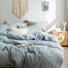 an unmade bed with blue sheets and pillows in a white room next to a window