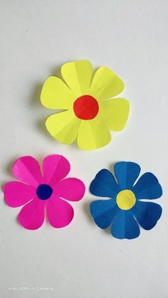 three different colored paper flowers on a white surface