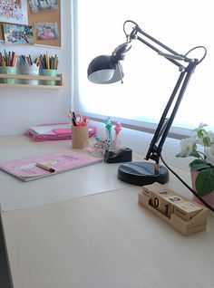 a desk with a lamp, books and other items on it in front of a window