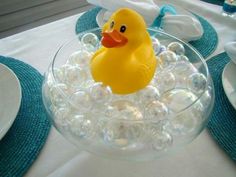 a rubber ducky floating in a bowl of bubbles on a table with plates and napkins