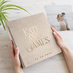 a person holding up a wedding album on a table next to a potted plant