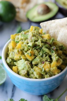 a blue bowl filled with guacamole and tortilla chips next to lime wedges